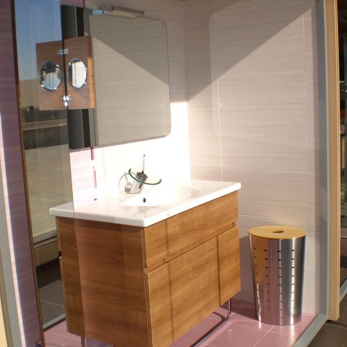 Baño completo en exposición con muebles en madera y sanitarios blancos